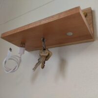 Houten plankje met drie magneten aan de onderzijde waar een sleutelbos en een telefoonkabel aan zin gehangen