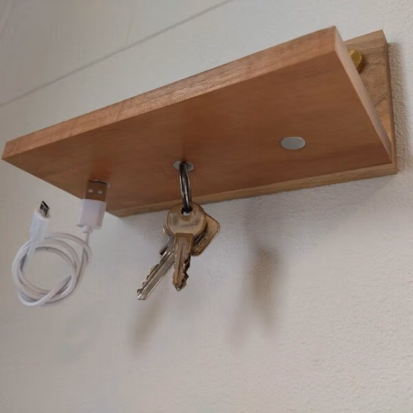 Houten plankje met drie magneten aan de onderzijde waar een sleutelbos en een telefoonkabel aan zin gehangen
