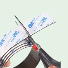 Hand die een stuk opgerold magneetband vasthoudt en een stukje afknipt met een schaar